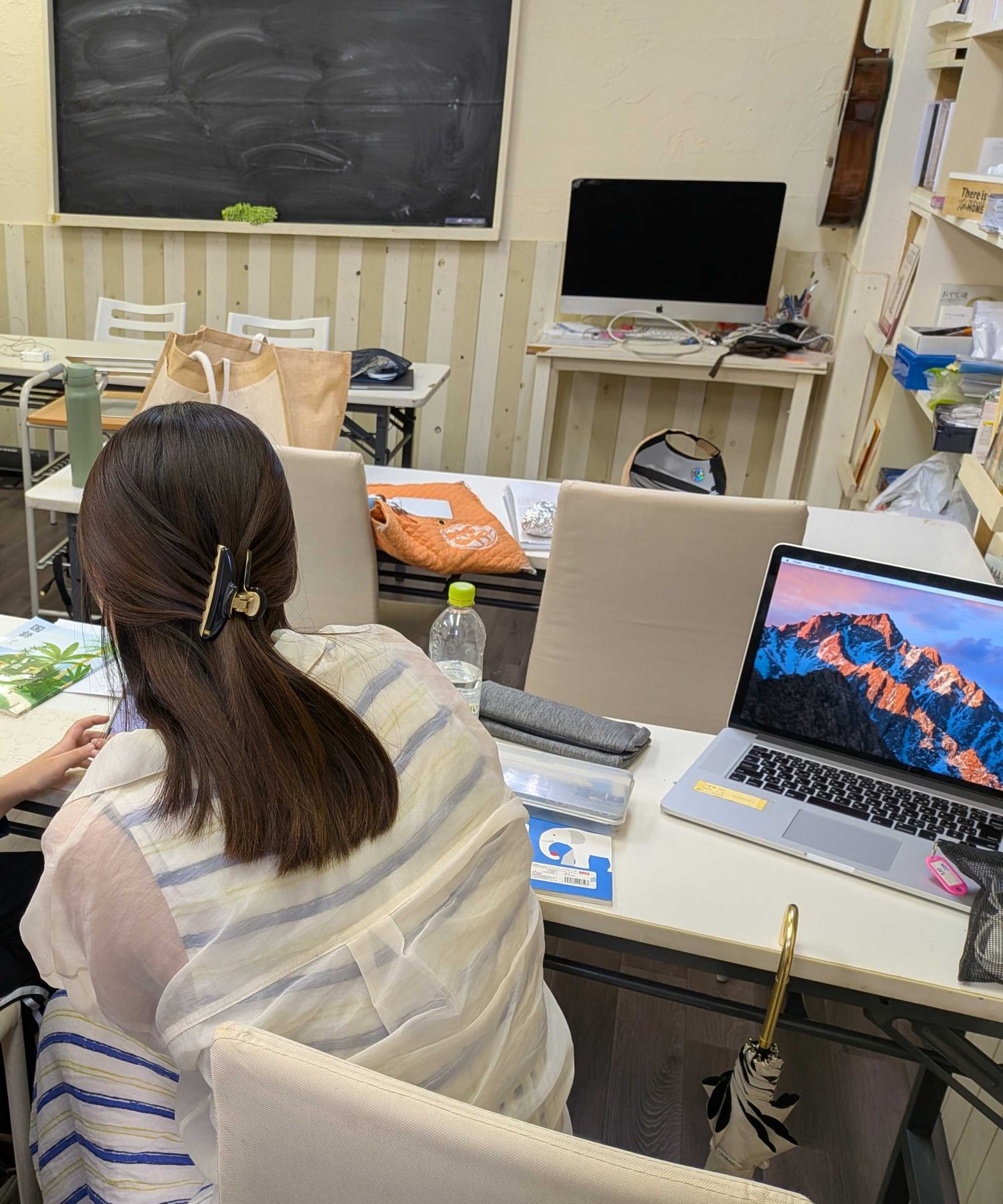 先生がとなりについて学習を見守る教室の様子（後ろ姿）
